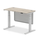 Grey oak Air 600mm deep height adjustable desk by Dynamic with cable ports and steel modesty panel, shown from a side angle.